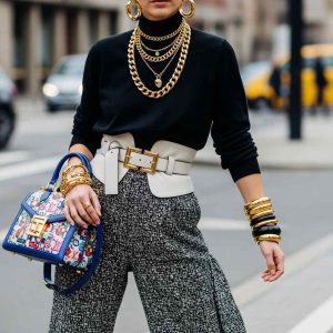 Fashion-forward outfit featuring bold statement accessories including chunky gold jewelry, a colorful designer handbag, layered necklaces, and a wide belt